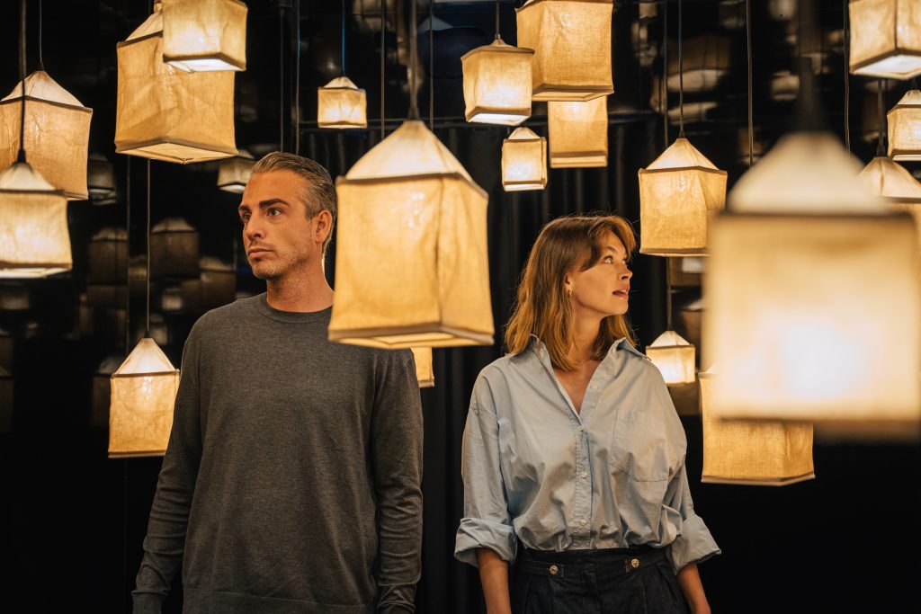A couple looking around an immersive room filled with warm hanging lanterns and dark reflective walls.